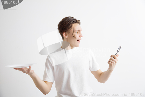 Image of Young smiling attractive guy holding empty dish and fork isolated on grey background.