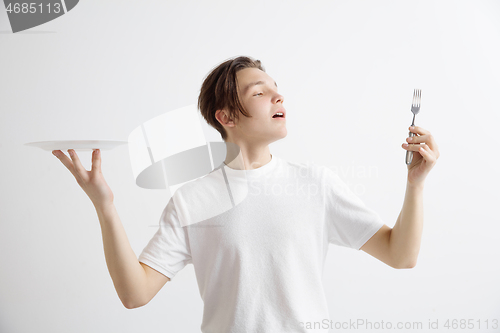 Image of Young smiling attractive guy holding empty dish and fork isolated on grey background.