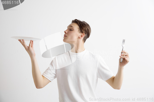 Image of Young smiling attractive guy holding empty dish and fork isolated on grey background.