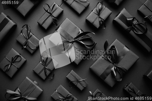 Image of Dark Christmas theme. Square boxed gifts wrapped in black paper and ribbon arranged on black