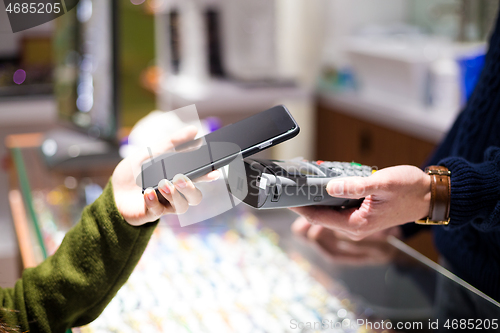 Image of Woman paying with NFC technology on smart phone at shop