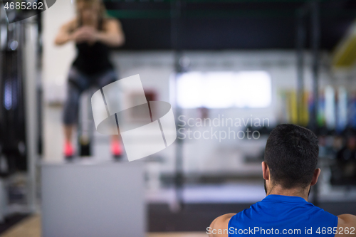 Image of woman working out with personal trainer jumping on fit box