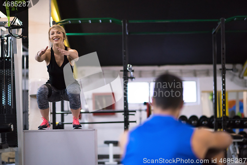 Image of woman working out with personal trainer jumping on fit box