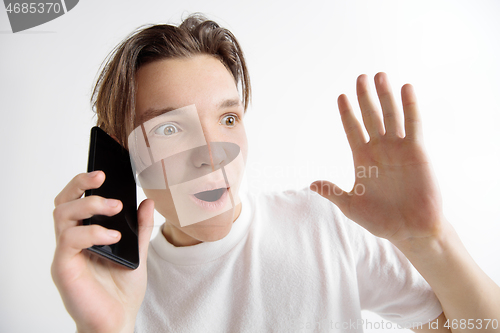 Image of Young handsome teenager showing smartphone screen isolated on gray background in shock with a surprise face
