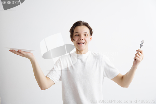 Image of Young smiling attractive guy holding empty dish and fork isolated on grey background.