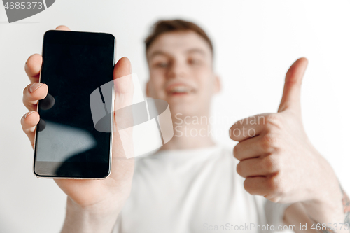 Image of Young handsome man showing smartphone screen and signing OK isolated on gray background