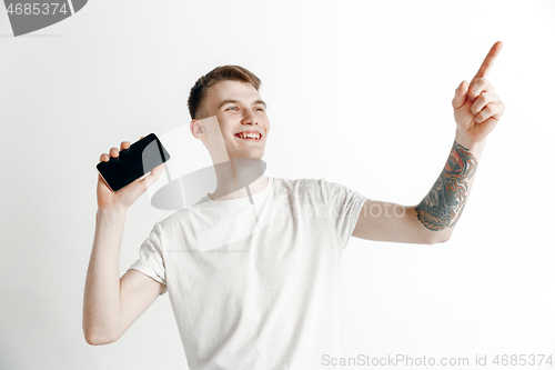 Image of Young handsome man showing smartphone screen and signing OK isolated on gray background