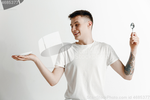 Image of Young smiling attractive guy holding empty dish and fork isolated on grey background.