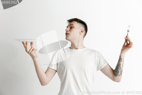 Image of Young smiling attractive guy holding empty dish and fork isolated on grey background.