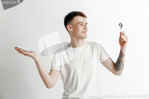 Image of Young smiling attractive guy holding empty dish and fork isolated on grey background.