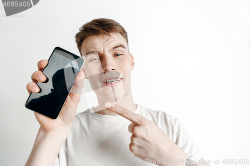 Image of Young handsome man showing smartphone screen and signing OK isolated on gray background