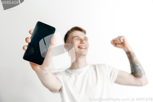 Image of Young handsome man showing smartphone screen and signing OK isolated on gray background