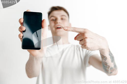 Image of Young handsome man showing smartphone screen and signing OK isolated on gray background