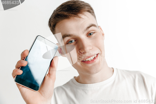 Image of Young handsome man showing smartphone screen and signing OK isolated on gray background