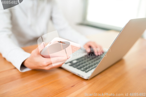 Image of Woman using laptop with cellphone