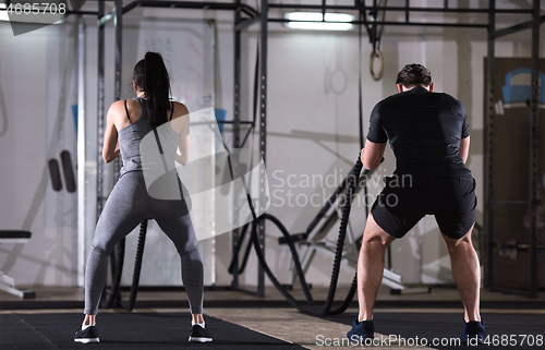 Image of sports couple doing battle ropes cross fitness exercise