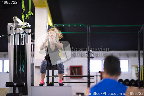 Image of woman working out with personal trainer jumping on fit box