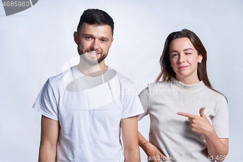 Image of Smiling couple standing over light background, joyful female pointing at guy and winking