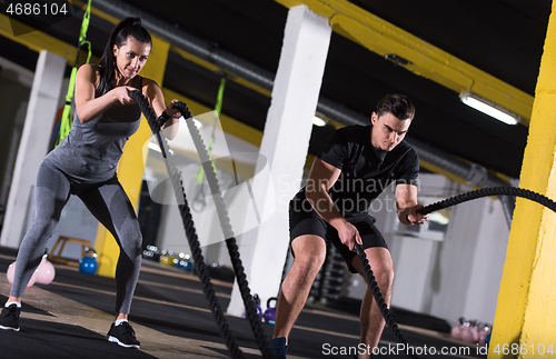 Image of sports couple doing battle ropes cross fitness exercise