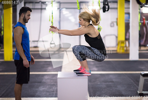 Image of woman working out with personal trainer jumping on fit box