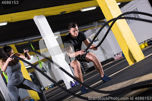 Image of sports couple doing battle ropes cross fitness exercise