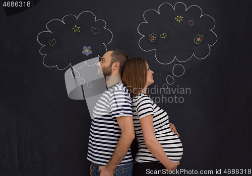 Image of pregnant couple posing against black chalk drawing board