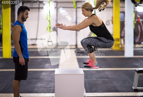 Image of woman working out with personal trainer jumping on fit box