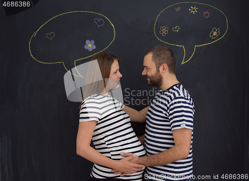 Image of pregnant couple posing against black chalk drawing board