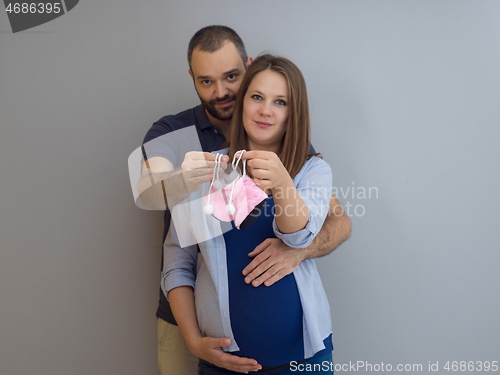 Image of pregnant couple holding newborn baby shoes