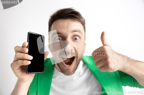 Image of Young handsome man showing smartphone screen and signing OK isolated on gray background