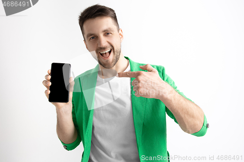 Image of Young handsome man showing smartphone screen and signing OK isolated on gray background