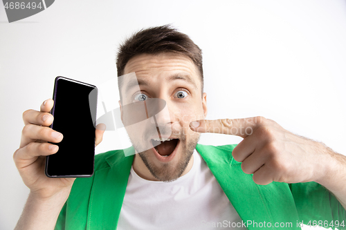 Image of Young handsome man showing smartphone screen and signing OK isolated on gray background