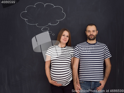 Image of pregnant couple posing against black chalk drawing board