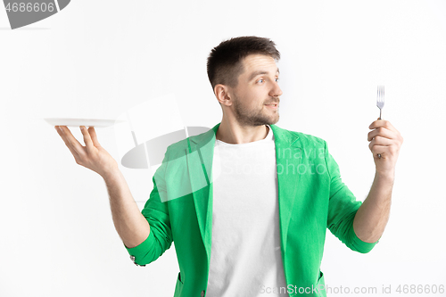 Image of Young smiling attractive guy holding empty dish and fork isolated on grey background.