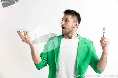 Image of Young smiling attractive guy holding empty dish and fork isolated on grey background.