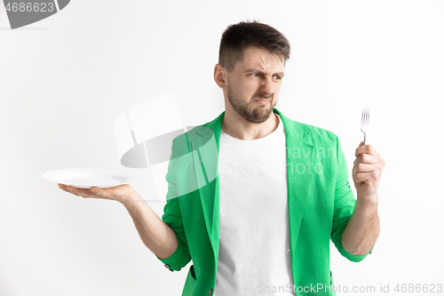 Image of Young sad attractive guy holding empty dish and fork isolated on grey background.