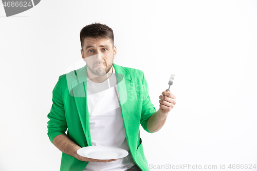 Image of Young sad attractive guy holding empty dish and fork isolated on grey background.