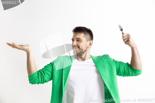 Image of Young smiling attractive guy holding empty dish and fork isolated on grey background.