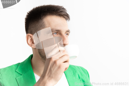 Image of Taking a coffee break. Handsome young man holding coffee cup, smiling while standing against gray background