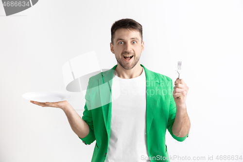 Image of Young smiling attractive guy holding empty dish and fork isolated on grey background.