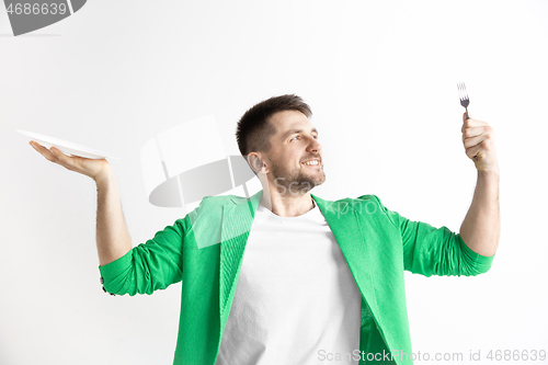 Image of Young smiling attractive guy holding empty dish and fork isolated on grey background.