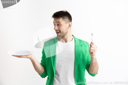 Image of Young smiling attractive guy holding empty dish and fork isolated on grey background.