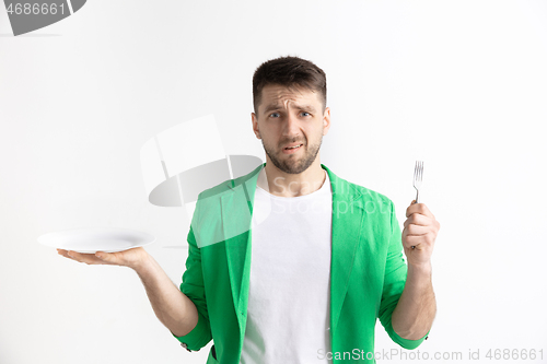 Image of Young sad attractive guy holding empty dish and fork isolated on grey background.