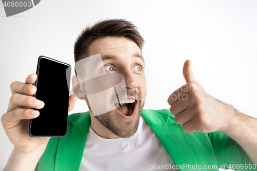 Image of Young handsome man showing smartphone screen and signing OK isolated on gray background