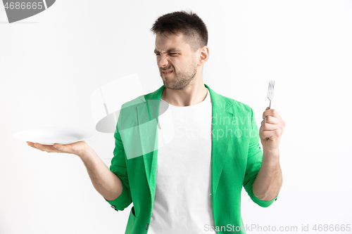 Image of Young sad attractive guy holding empty dish and fork isolated on grey background.