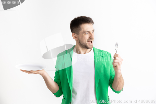 Image of Young smiling attractive guy holding empty dish and fork isolated on grey background.