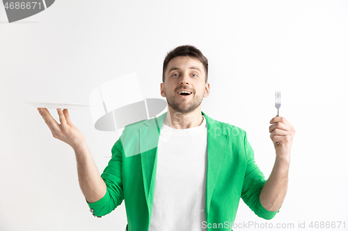 Image of Young smiling attractive guy holding empty dish and fork isolated on grey background.