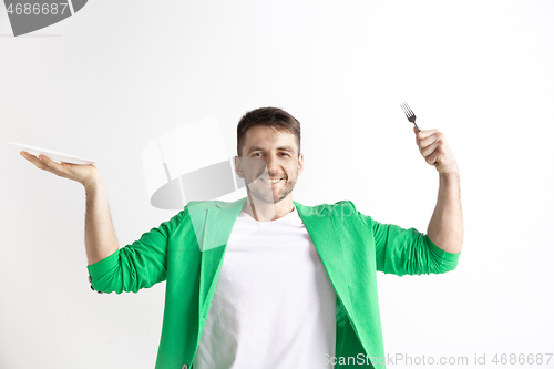 Image of Young smiling attractive guy holding empty dish and fork isolated on grey background.