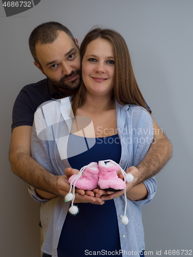 Image of pregnant couple holding newborn baby shoes