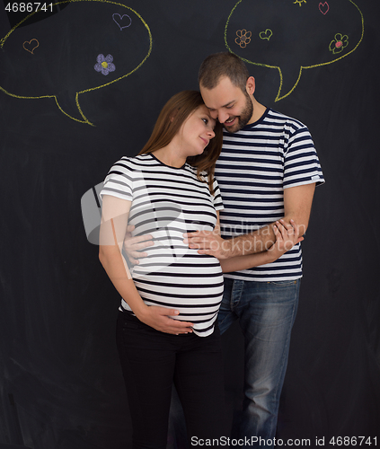 Image of pregnant couple posing against black chalk drawing board